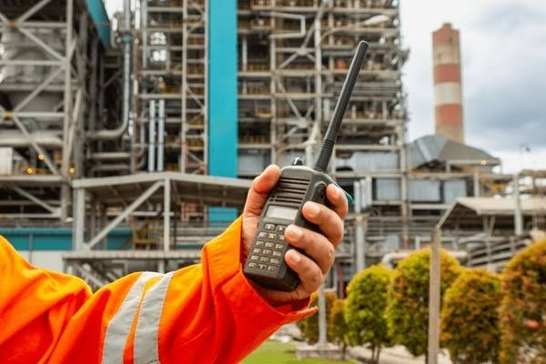 Operador em planta industrial segurando rádio robusto com sensores para segurança do trabalho.